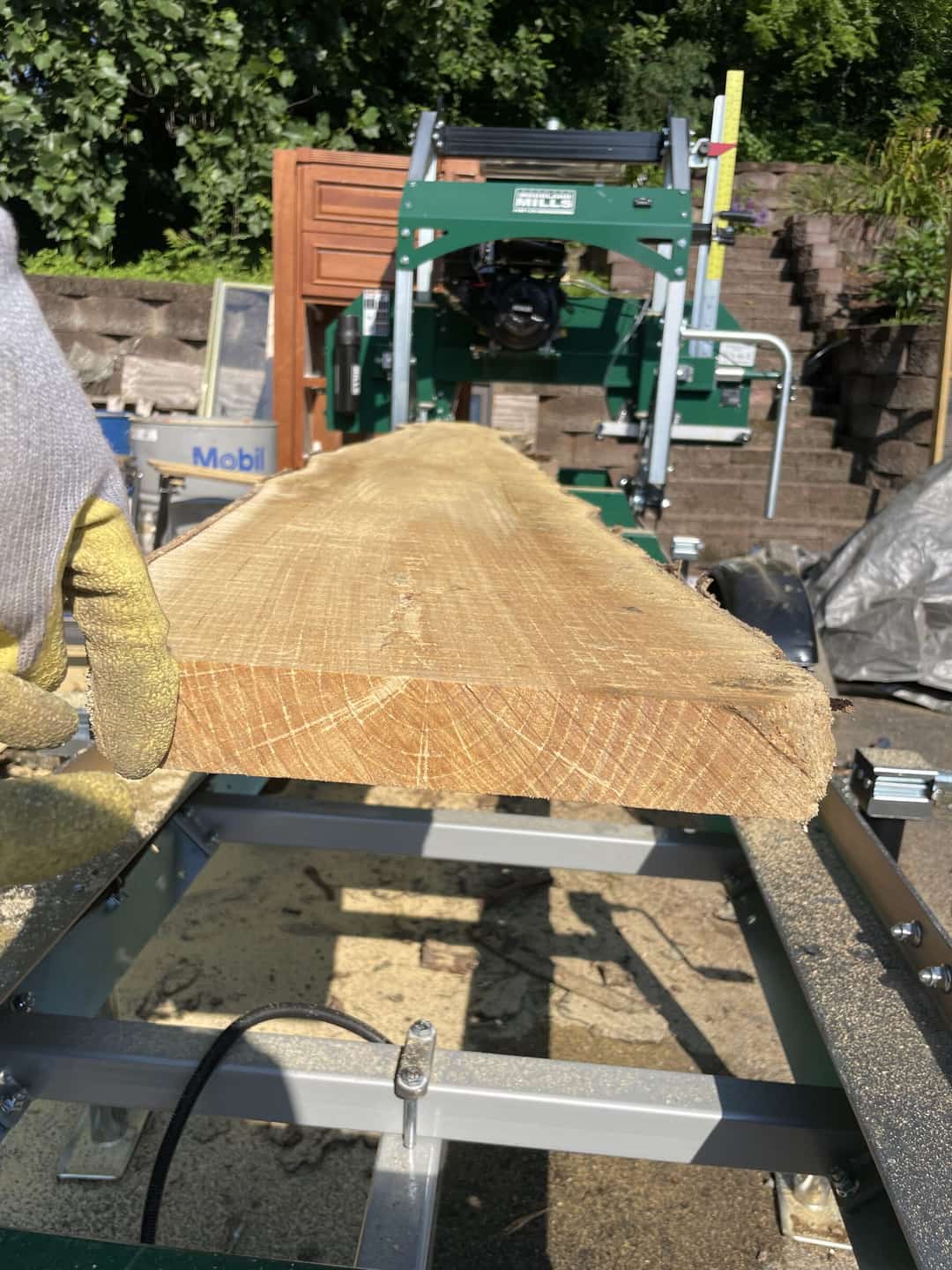A portable band sawmill part-way through a log, a gloved hand on the carriage.