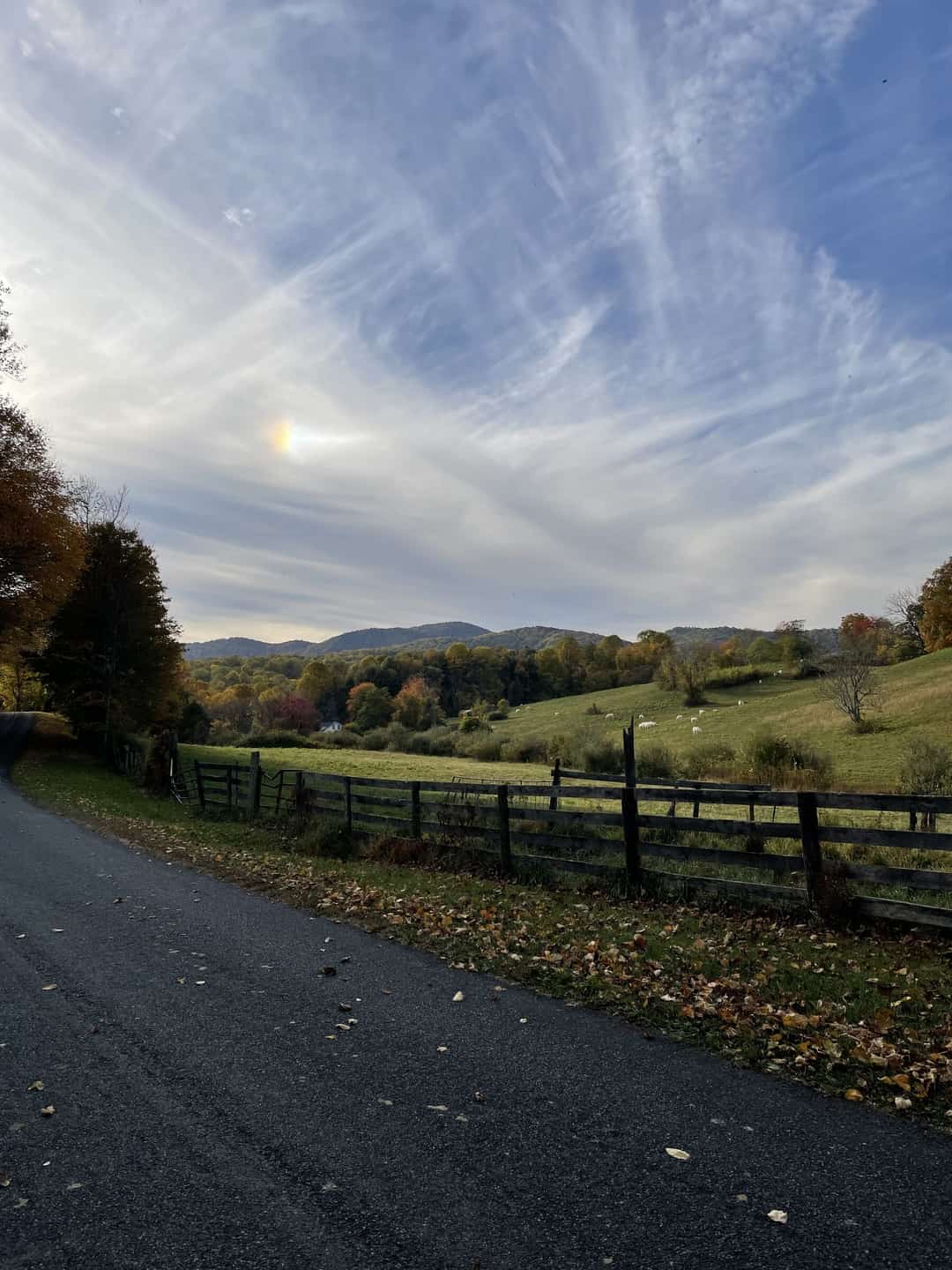 A country road in autumn, board fence along the shoulder and mountains beyond.