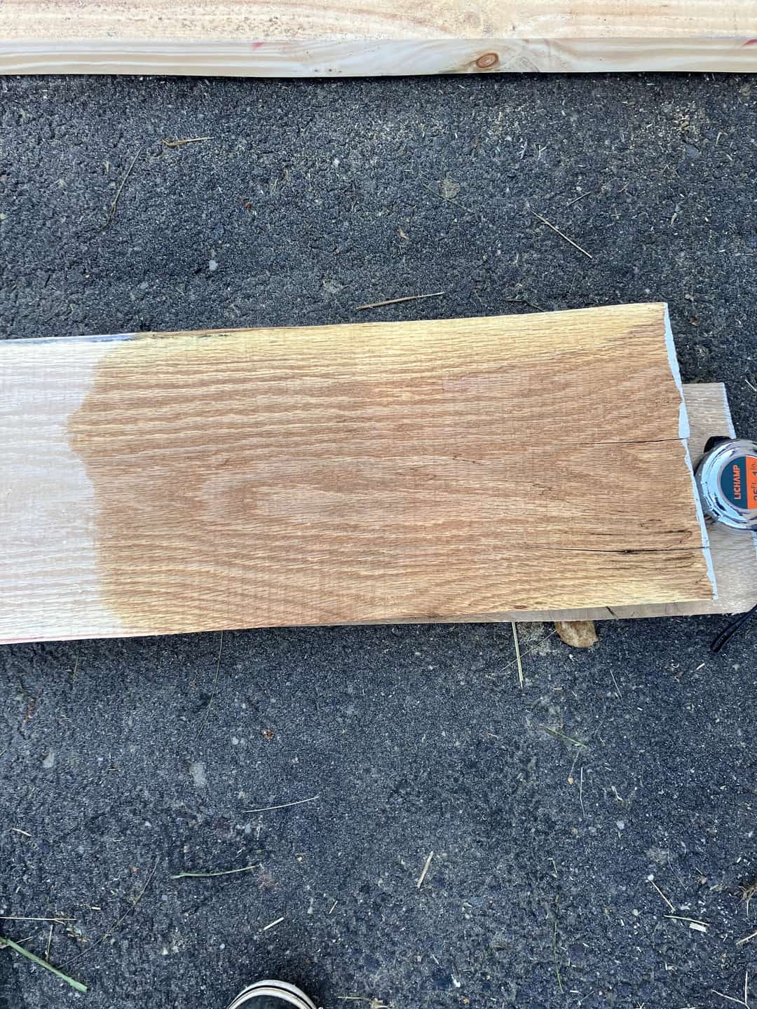 A freshly sawn board lying on gravel beside a tape measure.