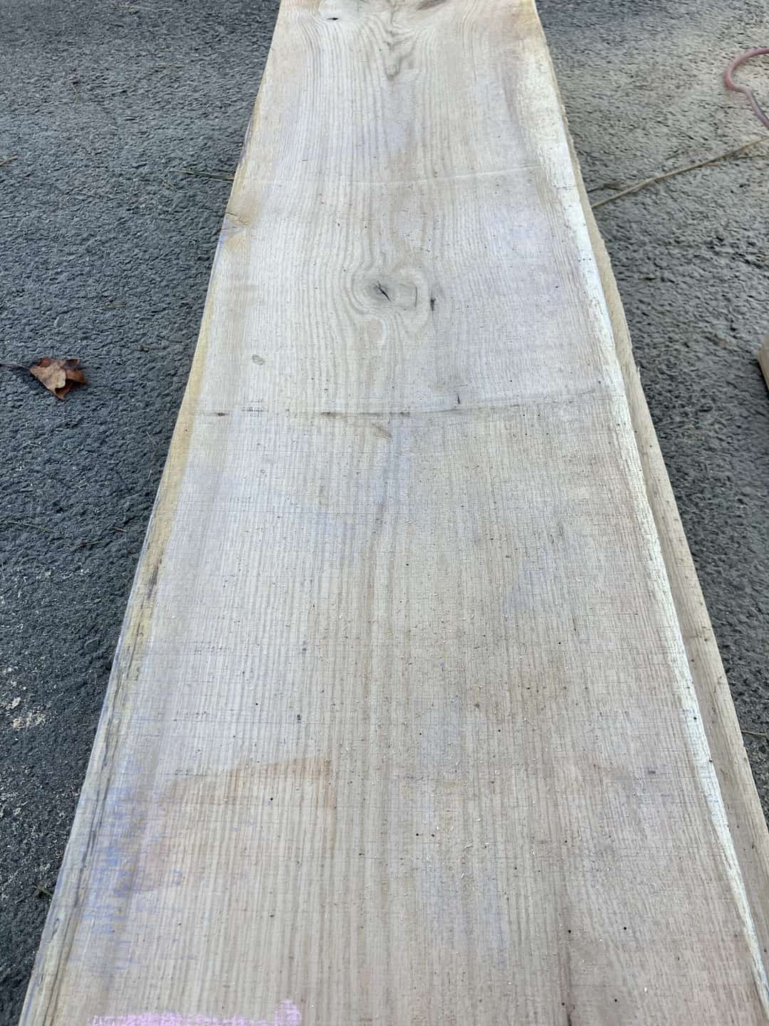 A wide sawn board tapering along its length, laid out on gravel.